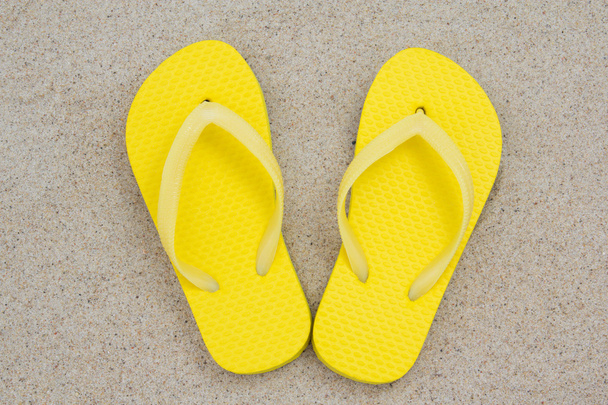 gele flip-flops op het zand - Foto, afbeelding