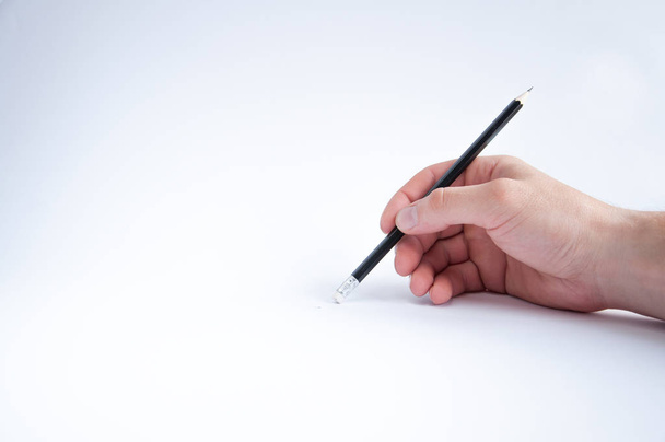 lápiz negro sostiene en su mano derecha. dibuja sobre un fondo blanco
 - Foto, Imagen