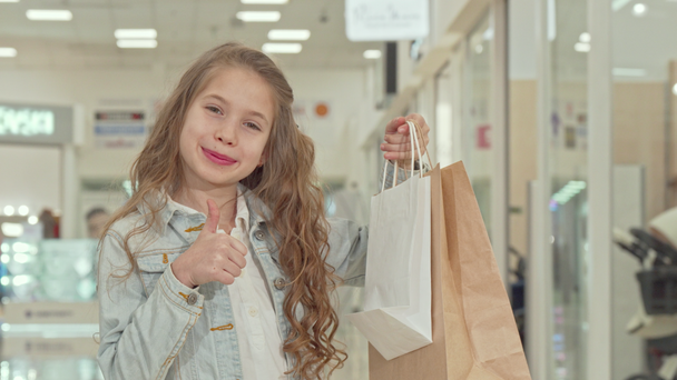 Šťastná roztomilá holčička ukazující palce v nákupním středisku - Záběry, video