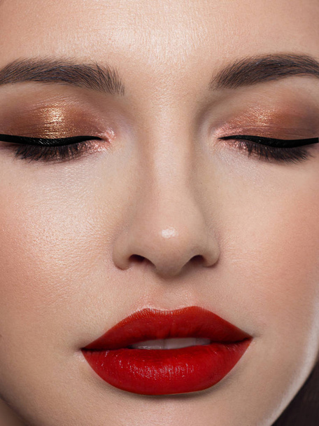 Close-up face of a girl with evening make-up. The arrows on the eyes and puffy lips scarlet. Thick eyebrows and eyelashes, perfect skin - Фото, изображение