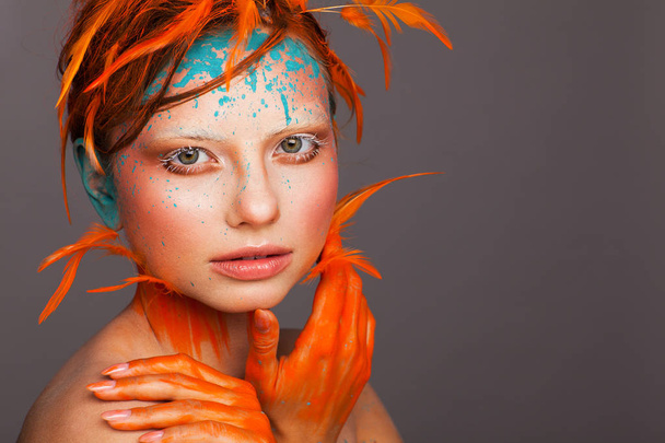 Portrait of a beautiful model with creative make-up and hairstyle using orange feathers - 写真・画像