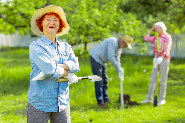 Cheerful retired woman with bright lips feeling happy taking care of garden - Фото, изображение
