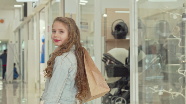 Happy Little Girl uśmiechając się do aparatu, trzymając worek na zakupy w centrum handlowym - Materiał filmowy, wideo