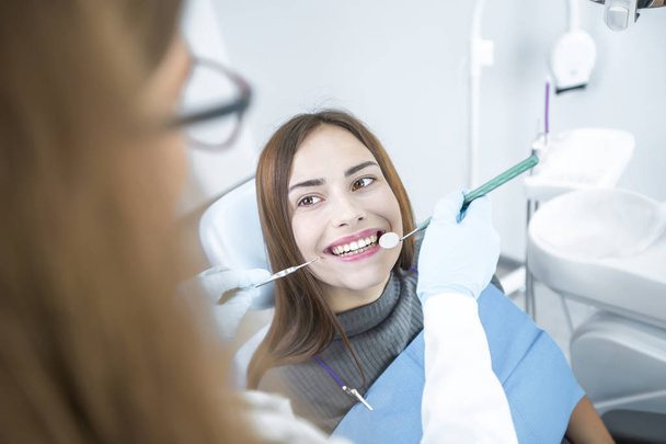 Lächelndes Mädchen behandelt Zähne, während es beim Arzt im Zahnarztstuhl sitzt.  - Foto, Bild