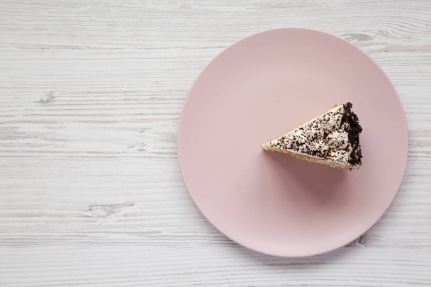 Un morceau de gâteau tiramisu sur une assiette rose sur une surfa blanche en bois
 - Photo, image