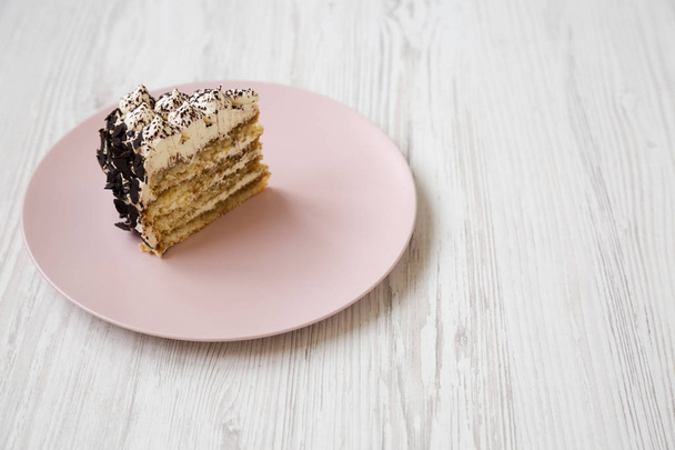 Um pedaço de bolo tiramisu em uma placa rosa em um backg de madeira branca
 - Foto, Imagem