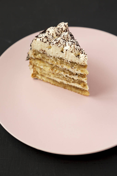 Un pedazo de pastel de tiramisú en un plato rosa sobre un fondo negro
,  - Foto, imagen