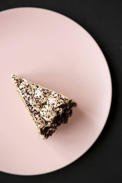 ein Stück Tiramisu-Kuchen auf einem rosa Teller vor schwarzem Hintergrund,  - Foto, Bild