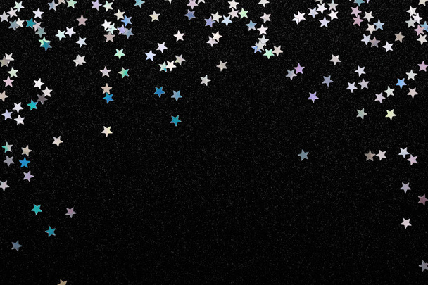 Iriserende zilveren sterren confetti op zwarte feestelijke achtergrond gloeiende schittert frame. - Foto, afbeelding