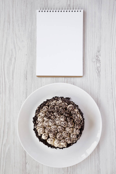 hausgemachter Tiramisu-Kuchen auf weißem Teller, leerer Notizblock auf weißem Papier - Foto, Bild