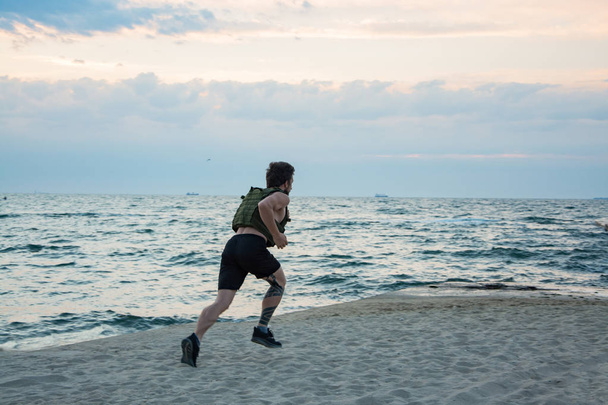 junger bärtiger Athlet trainiert im Freien mit gewichteter Weste, Übung mit militärischem Plattenträger - Foto, Bild