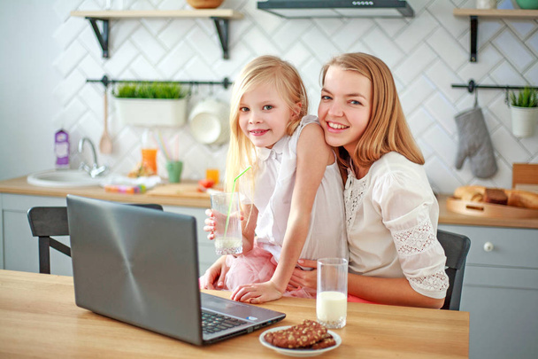 Mother with daughter sitting at table with groceries in kitchen - Foto, afbeelding