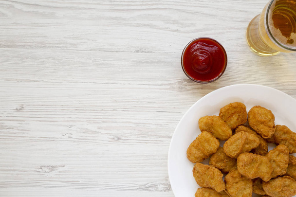 Chicken nuggets, ketchup and glass of cold beer on a white woode - Photo, Image