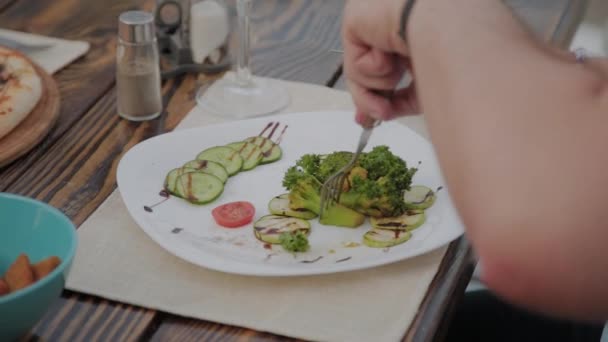Ένας νεαρός άντρας τρώει μεσημεριανό με μια σαλάτα με λαχανικά σε ένα εστιατόριο στην ανοιχτή βεράντα. Υγιεινό φαγητό. - Πλάνα, βίντεο