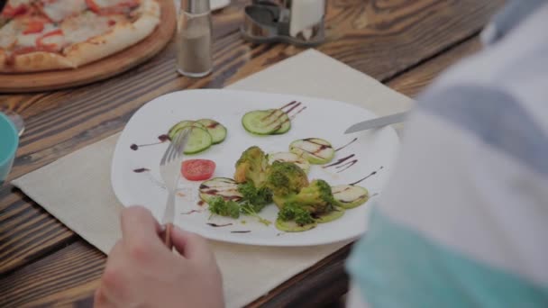 Een jongeman is lunchen met een salade met groenten in een restaurant op het open terras. Gezonde voeding. - Video