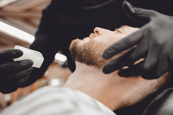 Barbeiro trata a pele da cara depois da barba perigosa com o sabão de bactérias, desinfecção na barbearia
 - Foto, Imagem