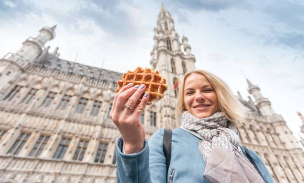 Młoda piękna kobieta trzyma tradycyjny belgijski wafel na tle wielkiego rynku w Brukseli, Belgia - Zdjęcie, obraz