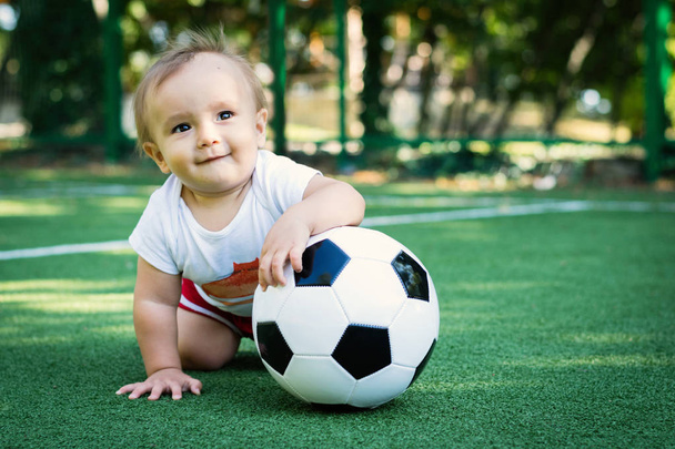 Dreaming little boy at the stadium with a soccer ball. Smiling toddler child on a sports ground with a ball. Future football star - Photo, image