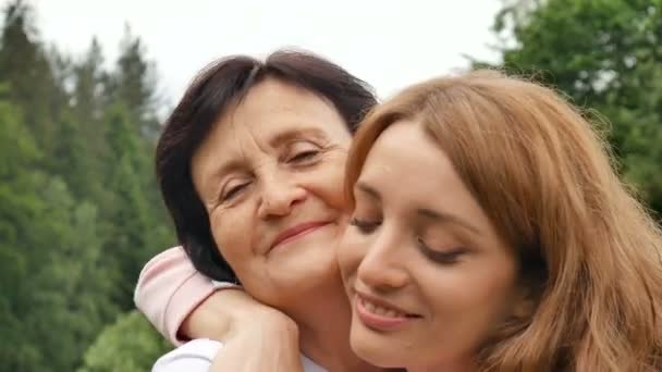 Na wolnym powietrzu zbliżenie portret z uśmiechnięty szczęśliwy kaukaski starszy matka z jej dorosły córka przytulanie i patrząc w The aparat fotograficzny. Dorosły córka pocałunki matka, dzień matki - Materiał filmowy, wideo
