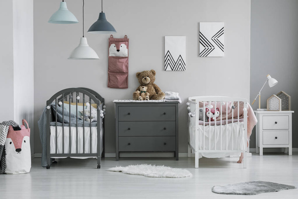 Brown teddy bear on grey wooden commode between two cribs in fashionable bedroom for twins - Foto, Imagen