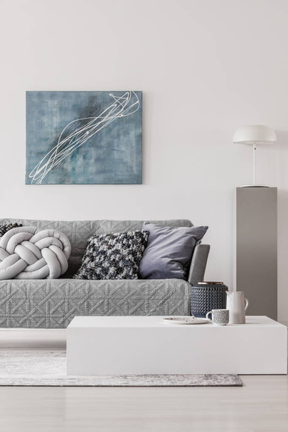 Blue abstract painting on white wall of contemporary living room interior with grey settee with pillows - Fotografie, Obrázek