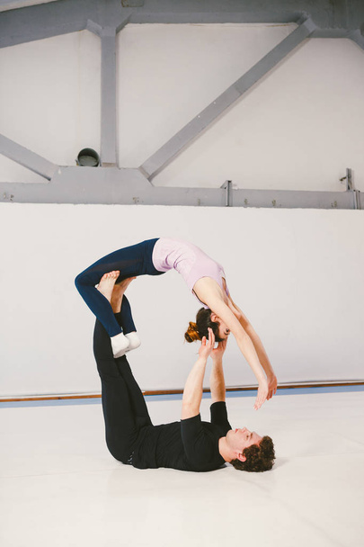 Young couple practicing akroyoga on a mat in the gym together. Woman flies. Man and woman sport training acrobatics yoga inside. Affiliate yoga, flexibility, trust concept. Teamwork - 写真・画像