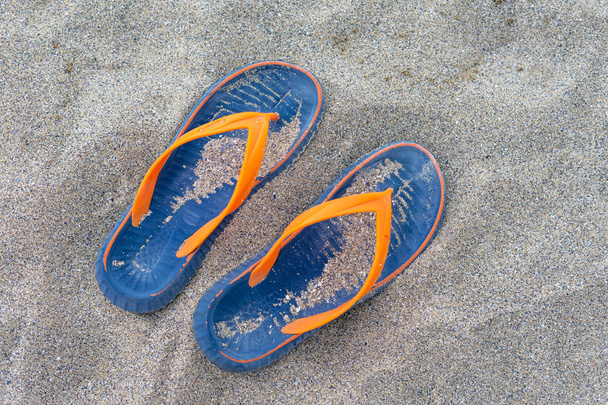 海の砂の上に青黄色のビーチスリッパ。コンセプト - 休息、リラクゼーション、旅行、ボート旅行. - 写真・画像