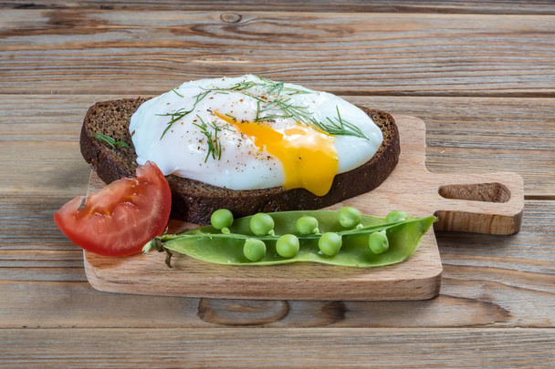 Top view of a poached egg with tomato and peas on wooden background - Photo, Image