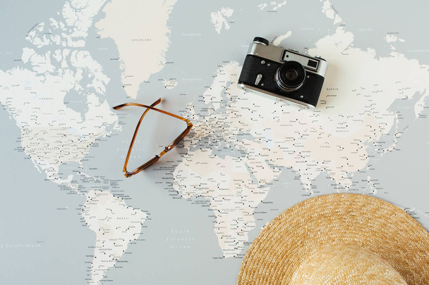 Minimal world map with pins, retro camera, sunglasses, straw hat. Flat lay vacation travel planning composition. Travel photographer concept. - Photo, image