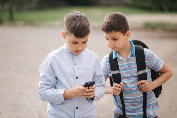 Δύο αγόρια παίζουν διαδικτυακά παιχνίδια μετά τα σχολικά μαθήματα. Νεαρά αγόρια χαμογελούν και χρησιμοποιούν το τηλέφωνο - Φωτογραφία, εικόνα