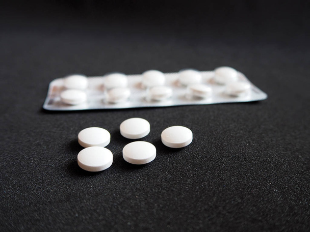 黒の背景に薬の丸薬と白いブリスターパック、病気を予防し、治療するために使用される近代的な薬。薬剤の包装:鎮痛剤,抗生物質,ビタミンやアスピリン錠.オピオイド流行と薬物乱用の概念。過剰摂取による自殺 - 写真・画像