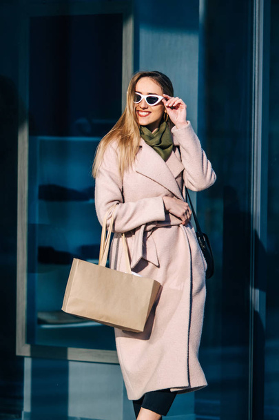 stylowa kobieta w płaszczu i okularach przeciwsłonecznych niedaleko sklepu - Zdjęcie, obraz
