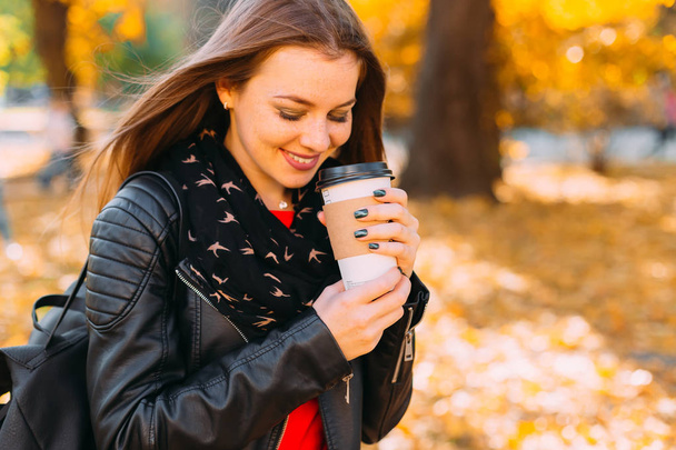 Portrét mladé dívky v kožené bundě a drží kávu cu - Fotografie, Obrázek
