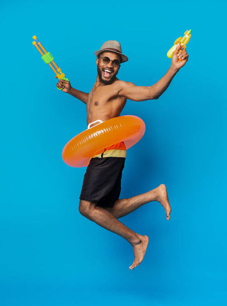水銃でジャンプする遊び心のある黒人男性 - 写真・画像