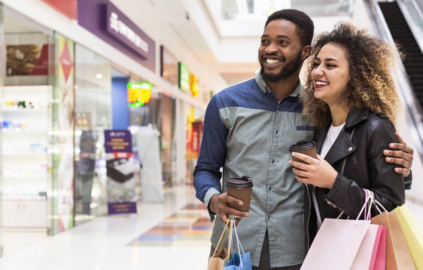 Feliz pareja africana sosteniendo bolsas de compras y mirando escaparate
 - Foto, imagen
