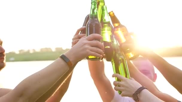 Grupo de jovens multiétnicos brindando com garrafas de cerveja e dançando à música ao pôr do sol, amigos bebem cerveja ao pôr do sol
 - Filmagem, Vídeo