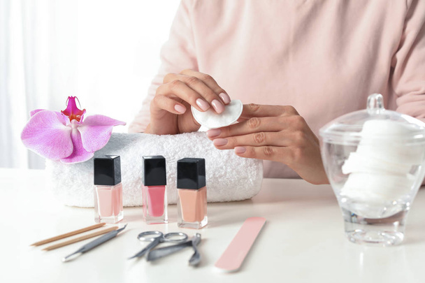 Woman removing polish from nails with cotton pad at table, closeup - Фото, изображение