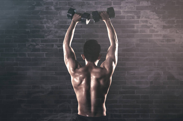 Back view of muscled man exercises with dumbbells - Foto, imagen