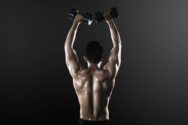 Вид сзади на мускулистого человека, поднимающего гантели
 - Фото, изображение