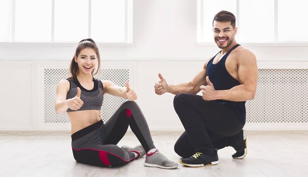 Young sporty couple sitting on floor with thumbs up - Photo, Image