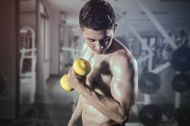 Muscled man lifts a dumbbell in the gym center - Photo, Image