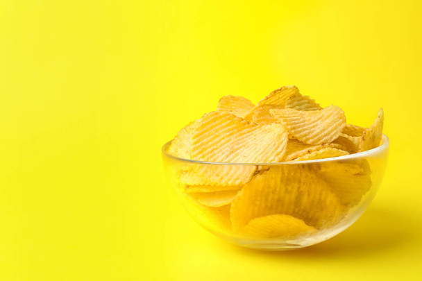 Delicious crispy potato chips in bowl on color background, space for text - Fotó, kép