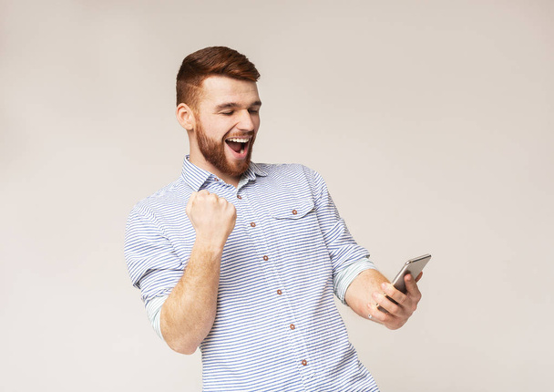 Radostný muž ukazující na znamení Yes a s pohledem na telefon - Fotografie, Obrázek