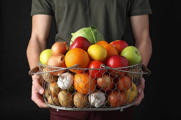 Man holding basket full of fresh  vegetables and fruits against black background, closeup - Fotó, kép