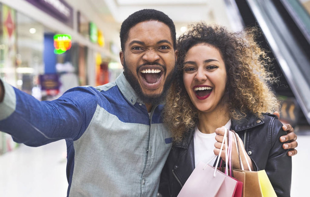 Feliz pareja africana haciendo selfie en el centro comercial con bolsas
 - Foto, imagen