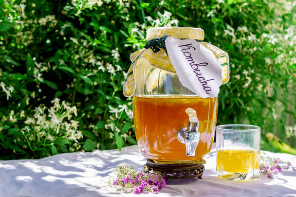 Frissítő Kombucha tea kakukkfű egy pohár régi Vintage üveg és egy pohár, a címke írásbeli Kombucha rajta a háttérben az elmosódott virágok. Egészséges természetes, probiotikus ízű ital. Lemezterület másolása - Fotó, kép