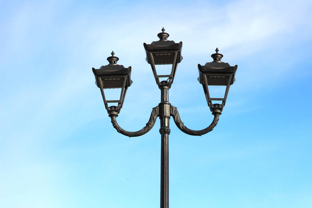 Foto von drei modernen Metall-LED-Lampen im Vintage-Stil auf einem einzigen Pfosten vor blauem Himmel - Foto, Bild