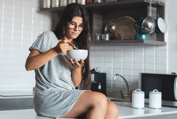 Young woman having breakfast in the kitchen - Foto, afbeelding