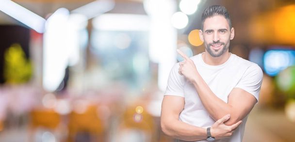 Handsome man wearing white t-shirt over night outdoors background Pointing with hand finger to the side showing advertisement, serious and calm face - Zdjęcie, obraz