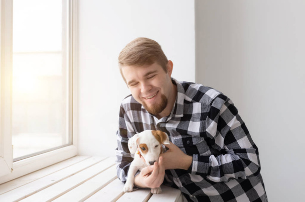 Άνθρωποι και κατοικίδιο ζώο ιδέα - ευτυχισμένος άνθρωπος κρατώντας ένα σκυλί Τζακ Ρασελ πάνω από το φόντο παράθυρο - Φωτογραφία, εικόνα